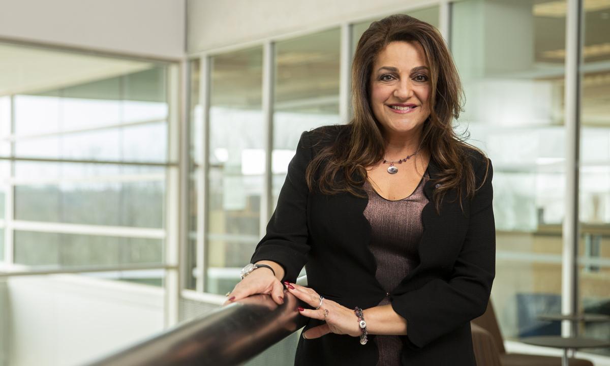 Photo of woman standing next to railing and smiling at camera