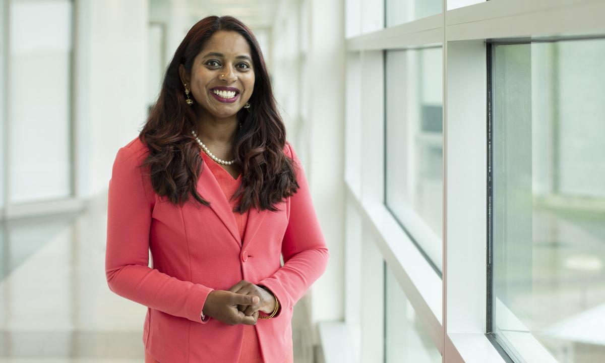 Image of a smiling female professor standing in a bright hallway